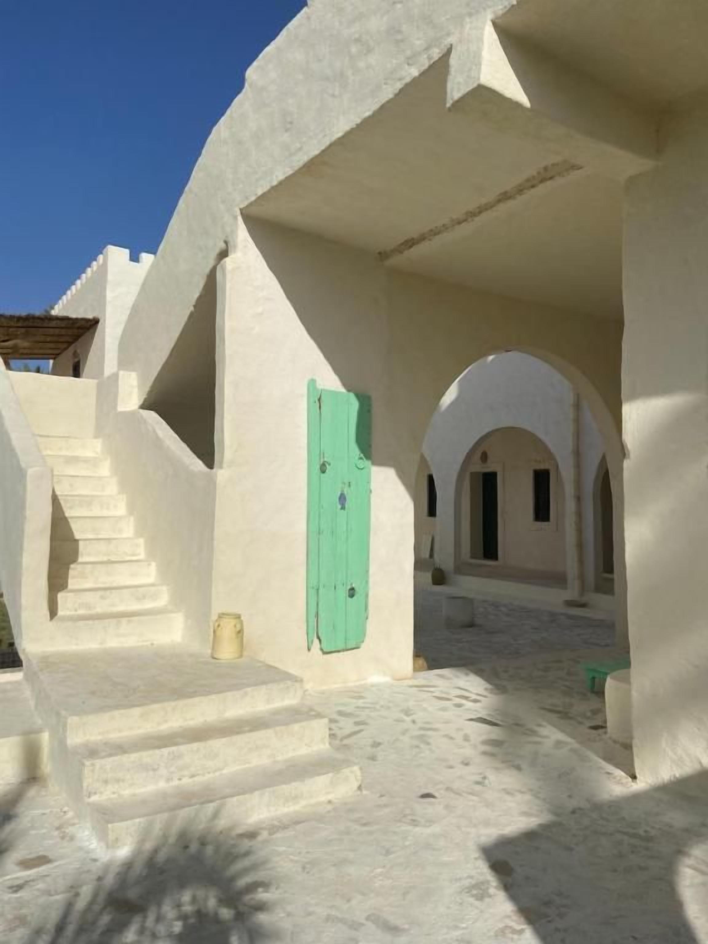 Un edificio con una escalera que conduce a un nivel superior, una puerta verde y un patio con cielo despejado.