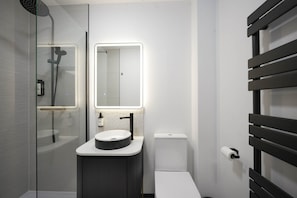 Uma casa de banho moderna com cabine de duche em vidro, uma sanita e lavatório branco com torneira preta.