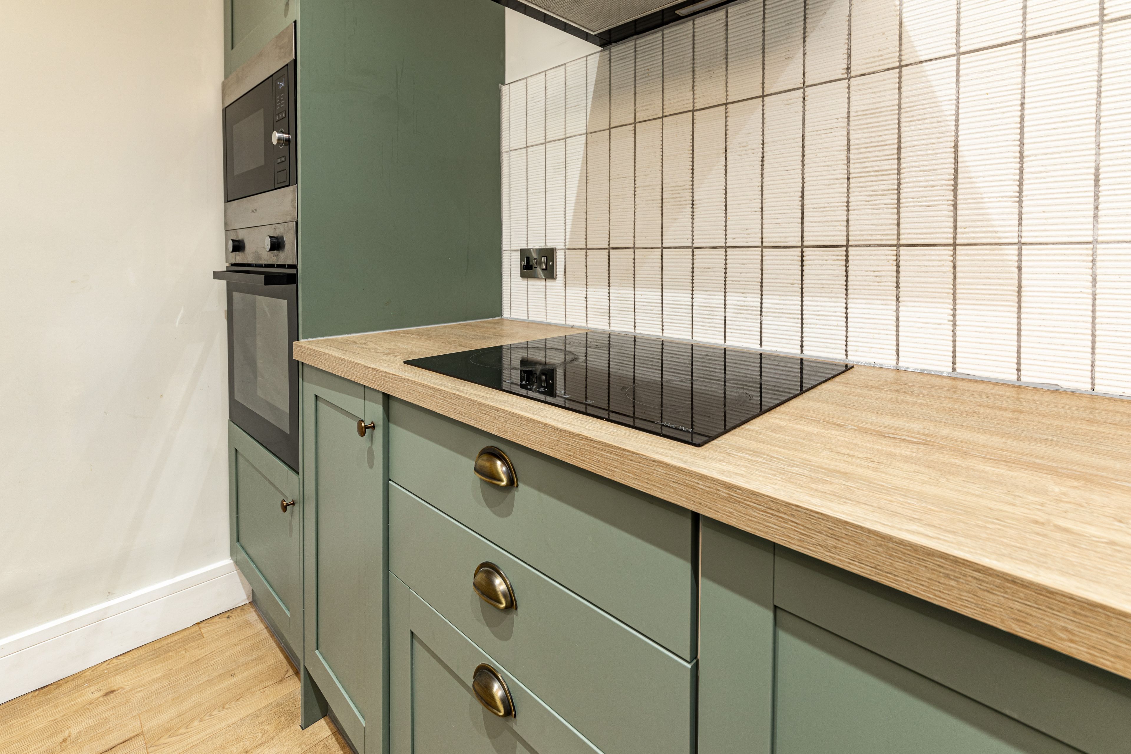 A kitchen with a built-in oven, a microwave, and a black induction cooktop on a wooden countertop.