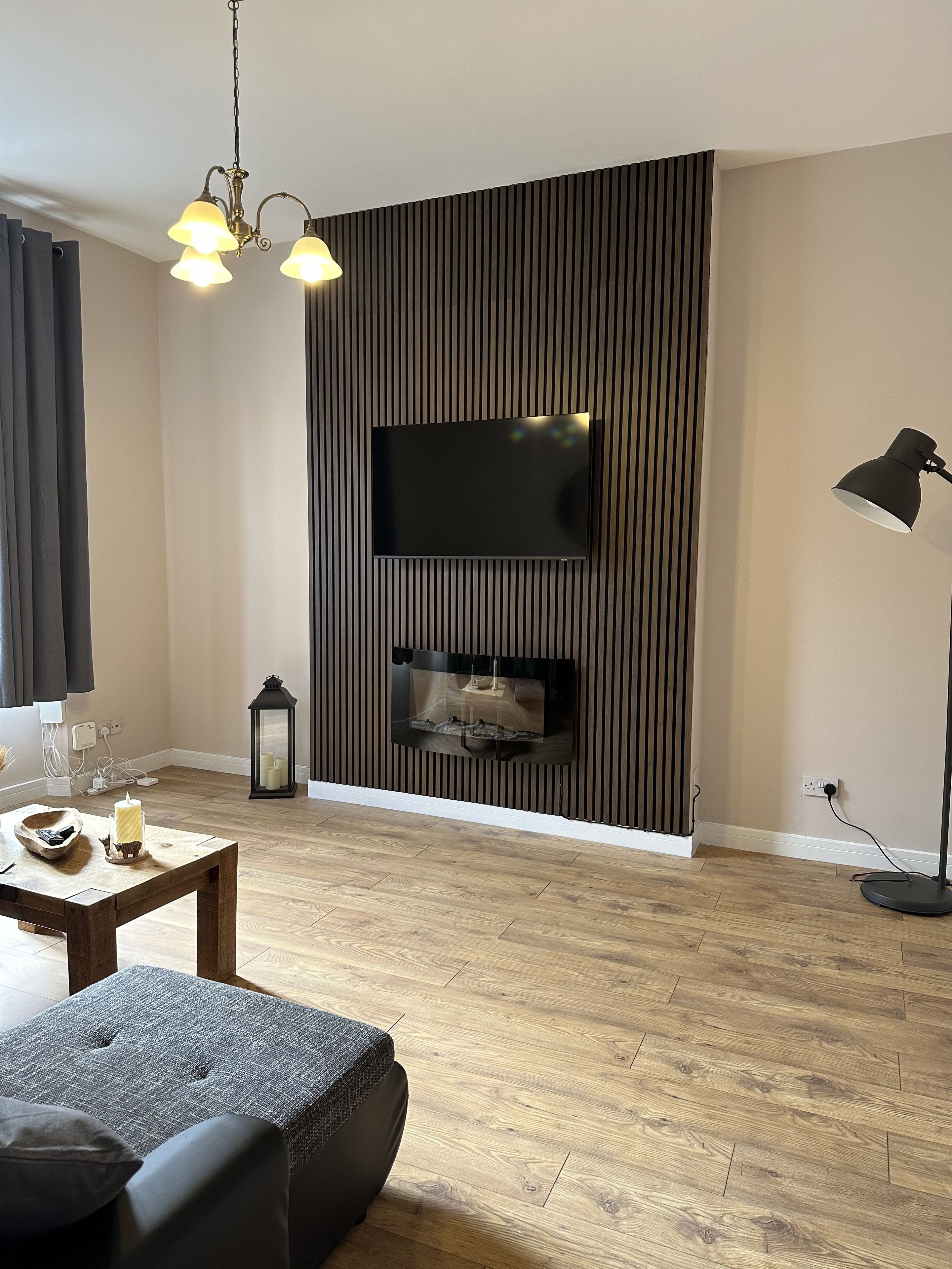A modern living room with a flat-screen TV mounted on a wall, a wooden floor, a dining table with chairs, and a floor lamp.