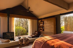 A bedroom with a large bed, a fireplace, a sofa, and a window with curtains.