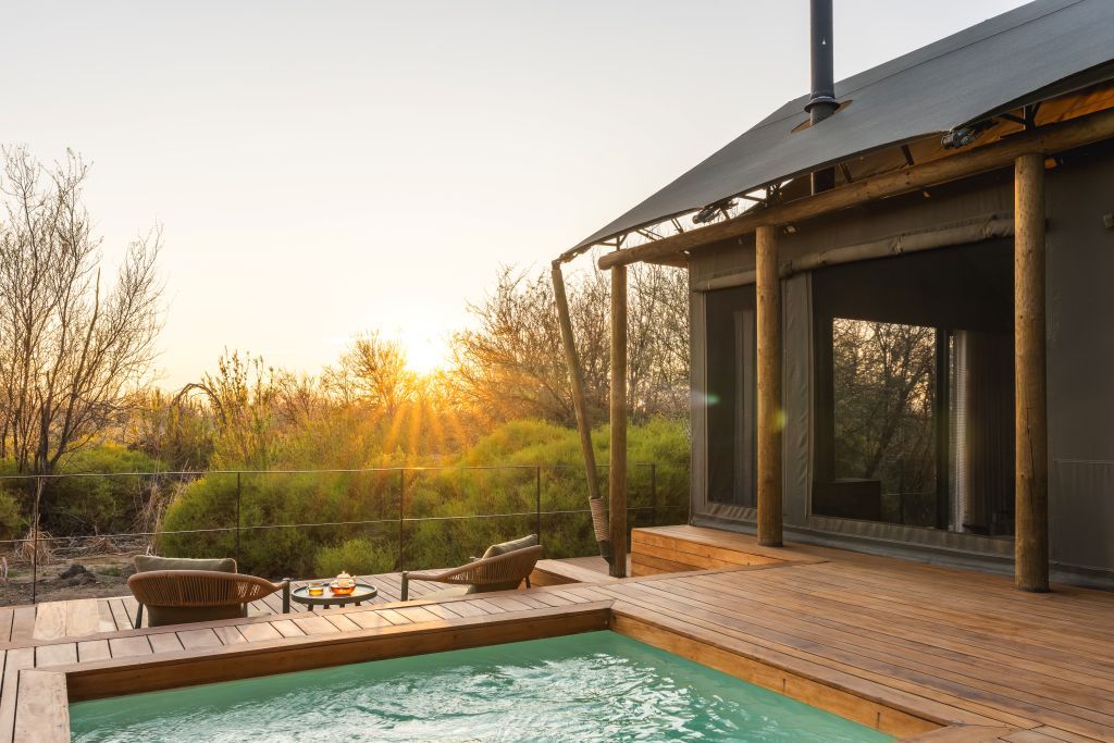 A wooden deck with a hot tub, wicker chairs, and a dining table.