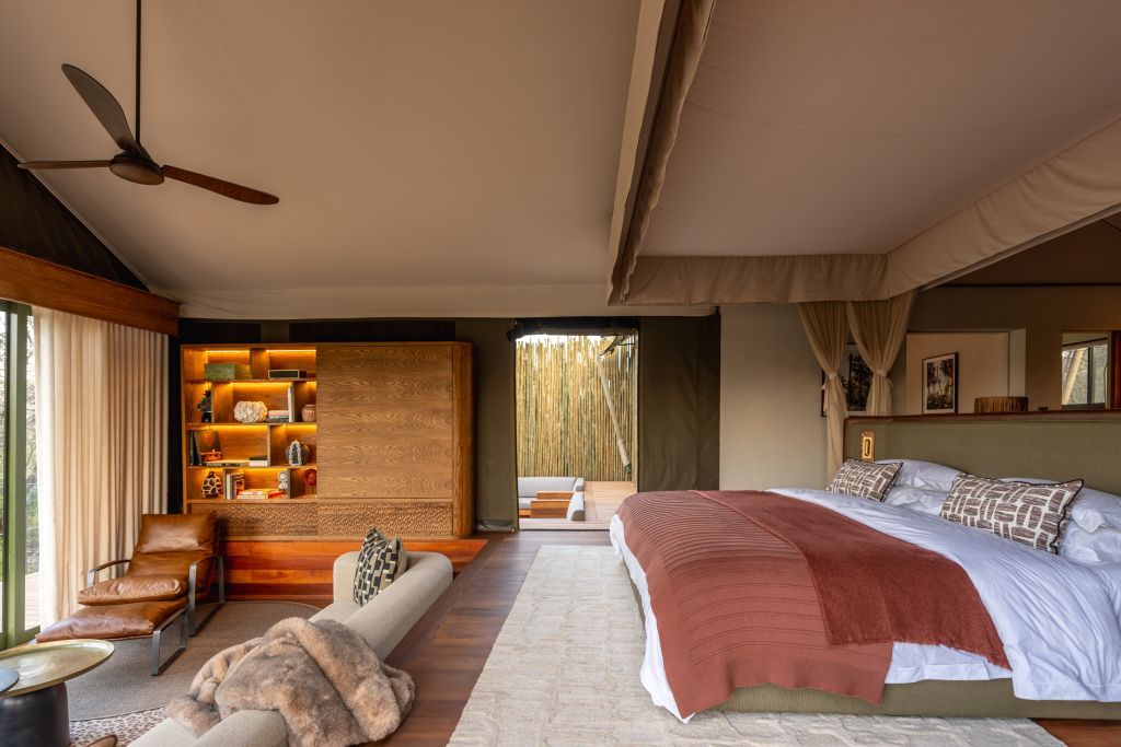 Un dormitorio con una cama grande, una zona de estar con sofá y sillón, una estantería de madera y un ventilador de techo.