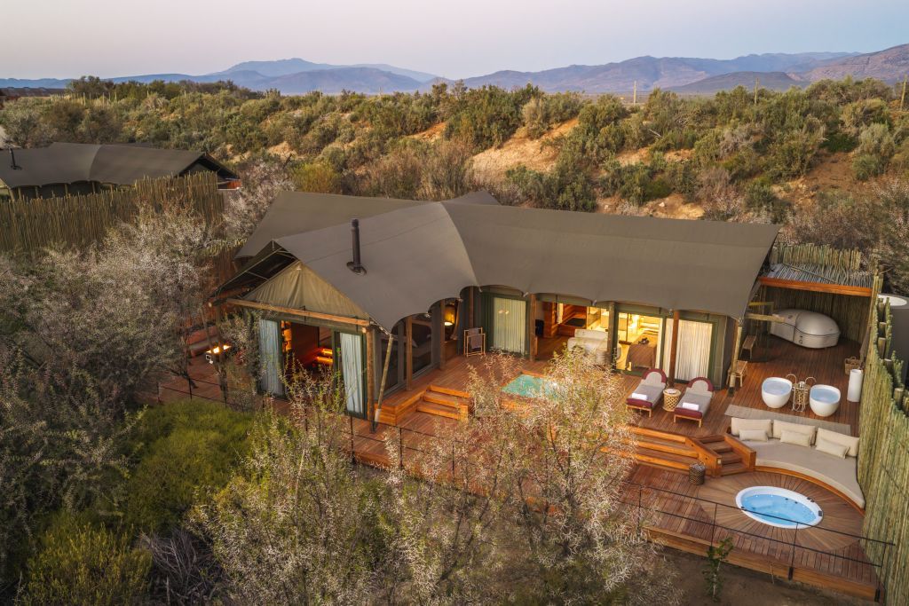 A secluded resort with a large outdoor pool, multiple guest rooms, and a scenic mountain backdrop.