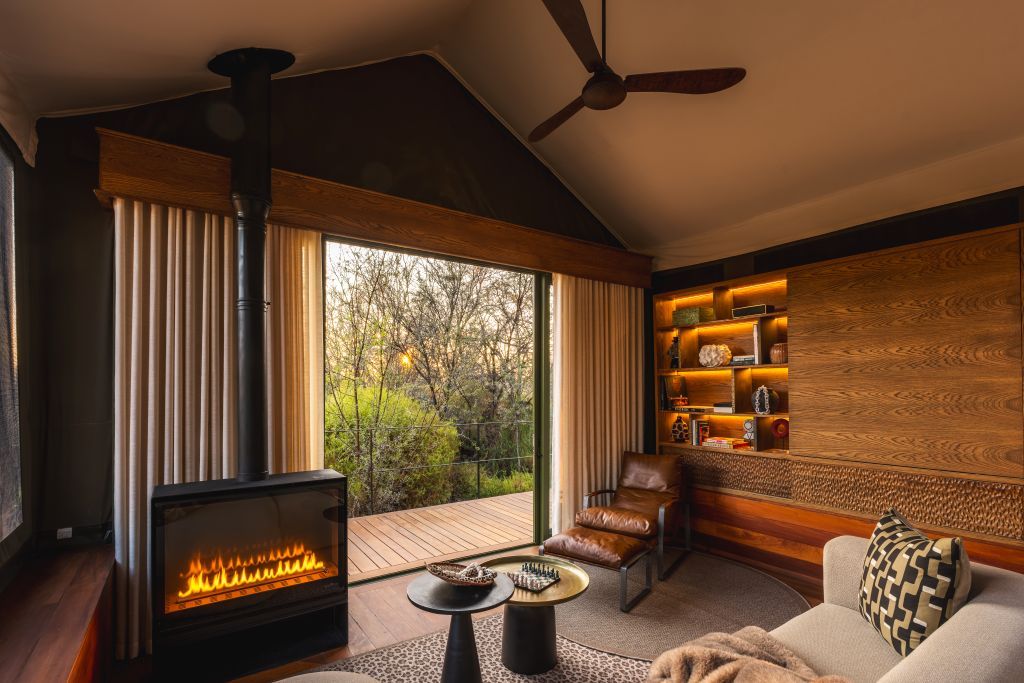 A modern living room with a fireplace, a ceiling fan, and a view of the outdoors.