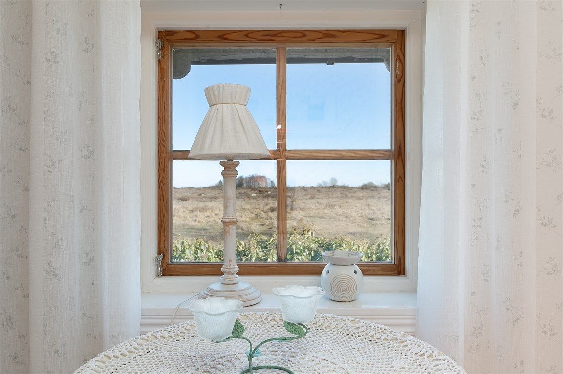 Et værelse med et vindue, et bord med hvide dug og en lampe.