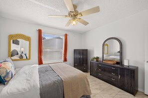 Ein Schlafzimmer mit Bett, Kommode, Spiegel und Deckenventilator.