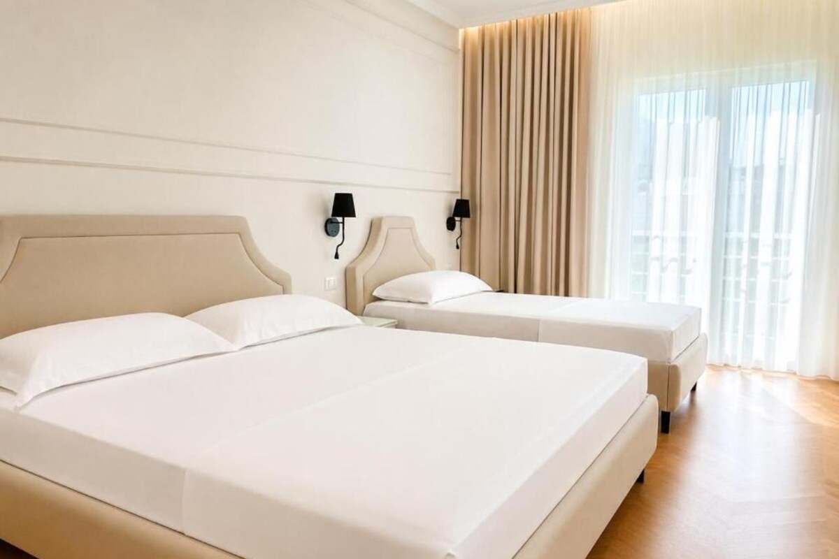 Una habitación de hotel con dos camas, un ventanal con cortinas y piso de color claro.