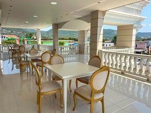 Un comedor con mesas y sillas, un balcón con barandilla y vistas al paisaje.