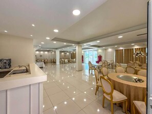 Een ruime hotel eetruimte met meerdere tafels en stoelen, een receptiebalie en een modern interieur.