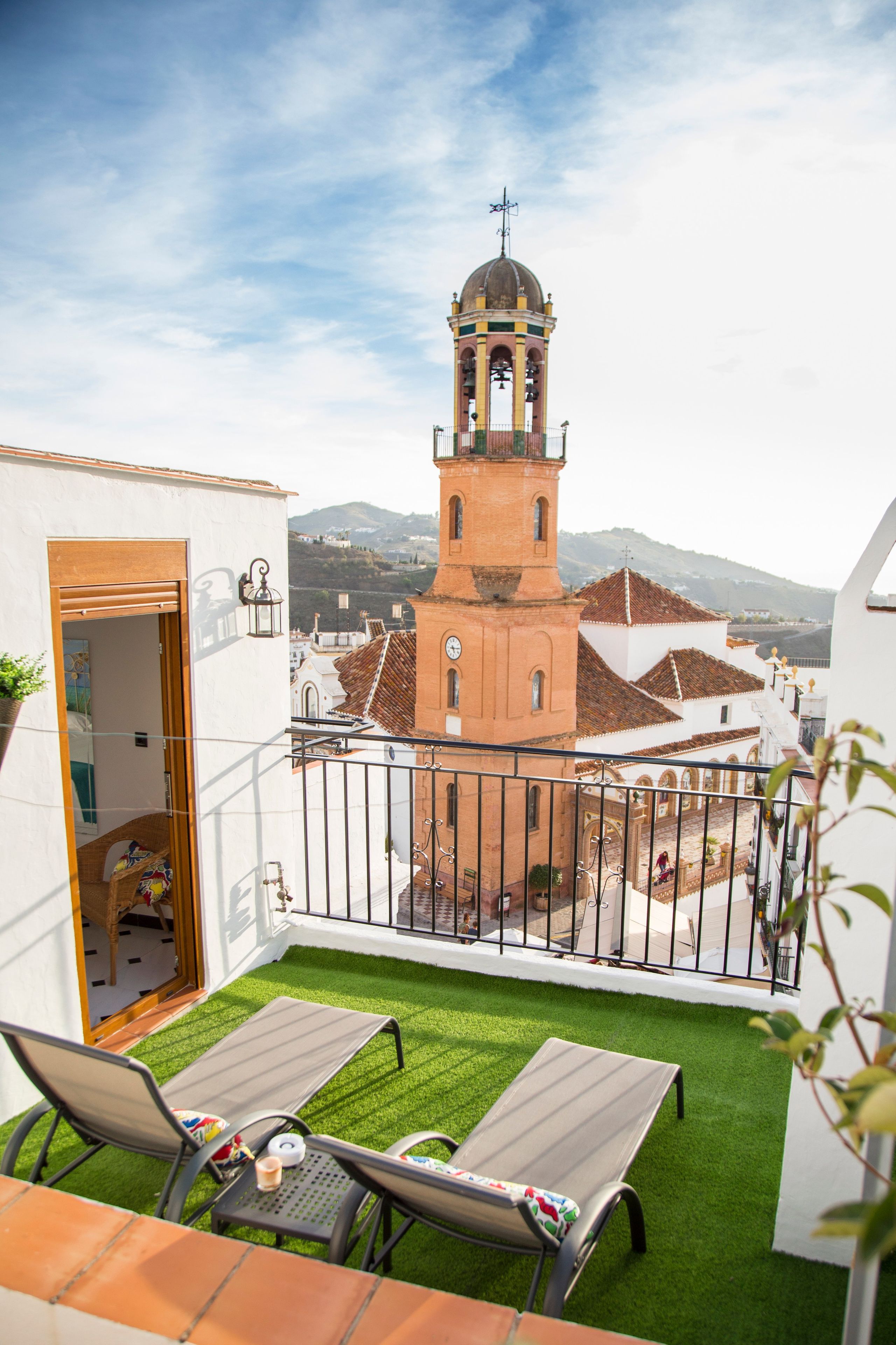 Un balcon agrémenté de gazon synthétique, deux fauteuils de jardin, une petite table et une vue sur une tour historique en arrière-plan.