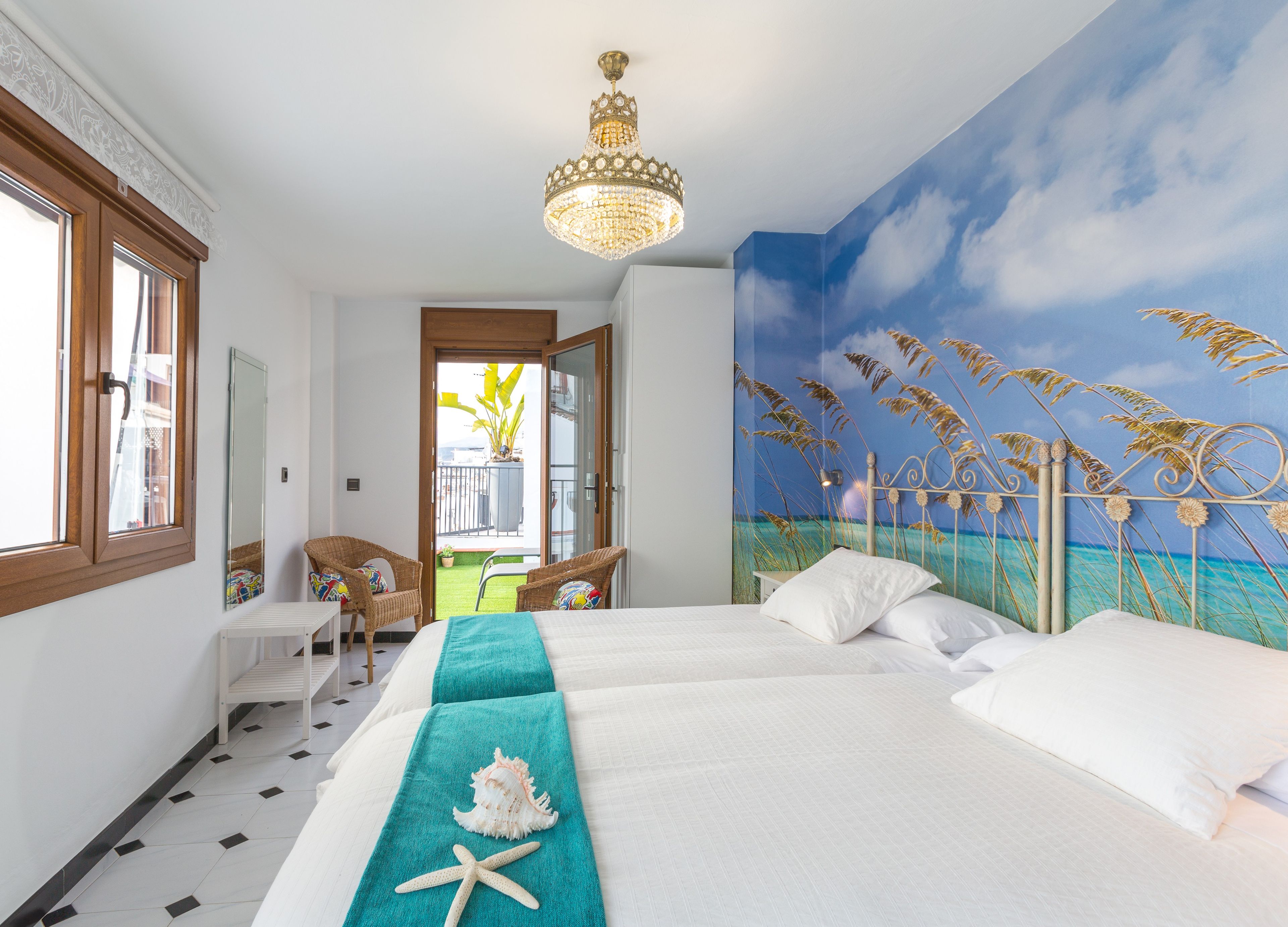 Une chambre d’hôtel avec un lit, un balcon, un lustre et une fresque représentant une scène de plage.