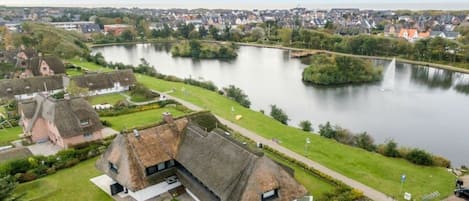 Une propriété située au bord de la rivière, avec un bâtiment à toiture de chaume, un espace de stationnement et une vue sur une ville de l’autre côté de l’eau.