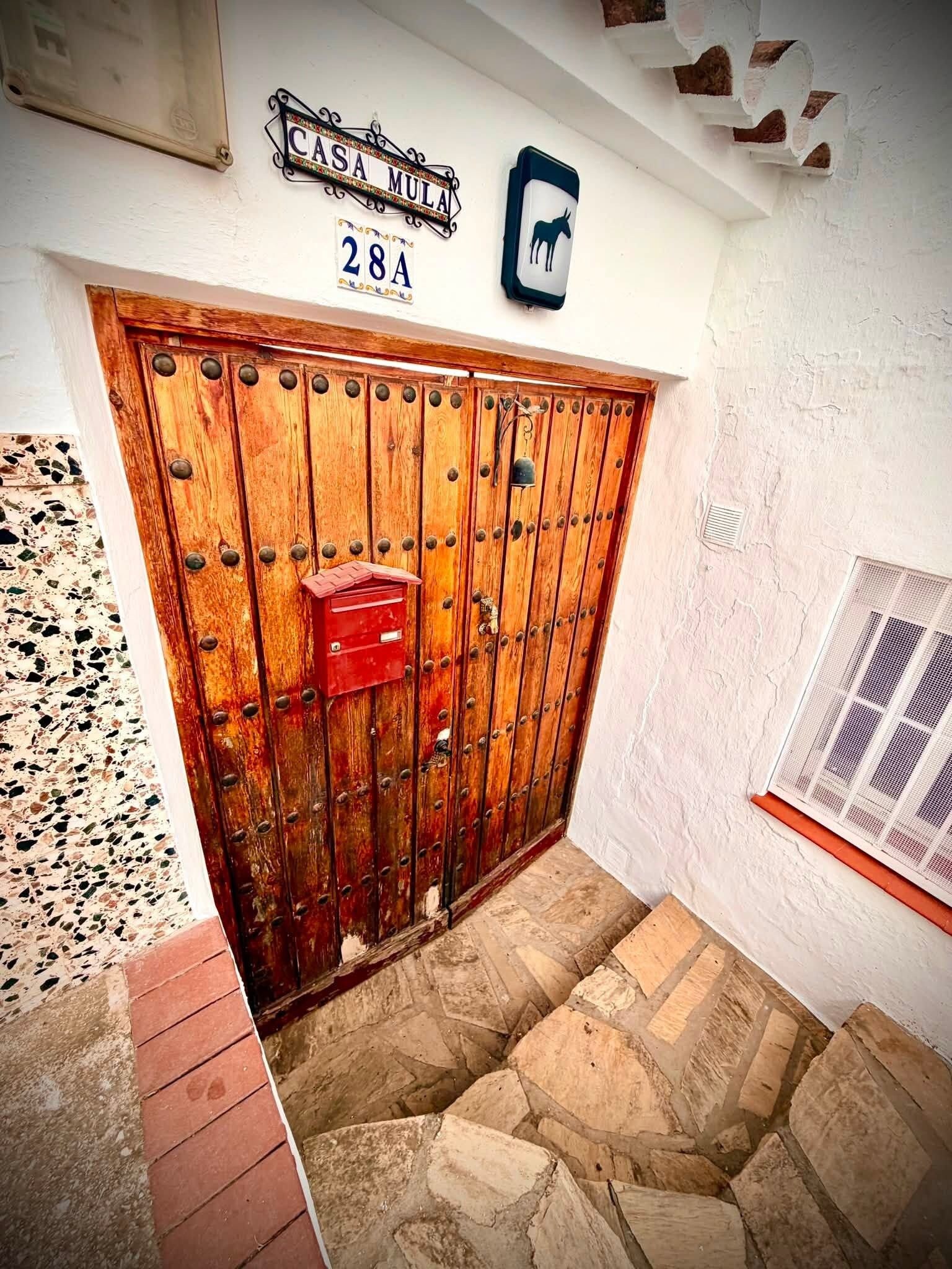 Una puerta de madera rústica con un buzón, una señal de calle arriba y un suelo de piedra.