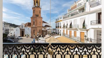 Vista de una plaza de pueblo con una imponente torre de iglesia, un edificio blanco con balcones y un cielo despejado.