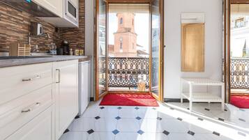 Une cuisine moderne équipée d’un four à micro-ondes, d’une machine à café et agrémentée d’un tapis rouge menant à un balcon d’où l’on peut admirer le clocher d’une église.