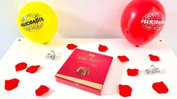 Ein Tisch mit einer roten Schachtel mit dem Aufdruck 'Caja Roja' und zwei Ballons mit der Aufschrift 'FELICIDADES'.