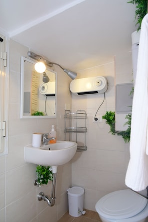 Een badkamer met een witte wastafel, spiegel en toilet. Een haardroger en handdoekhouder zitten op de muur.