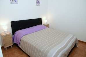 Een bed met een gestreept dekbedovertrek, twee bedlampjes en een nachtkastje met een lamp.