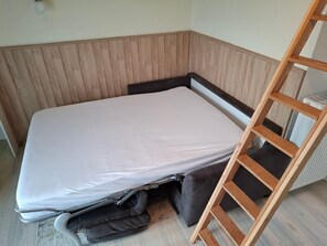 Habitació petita amb un llit, una escala de fusta i un radiador.