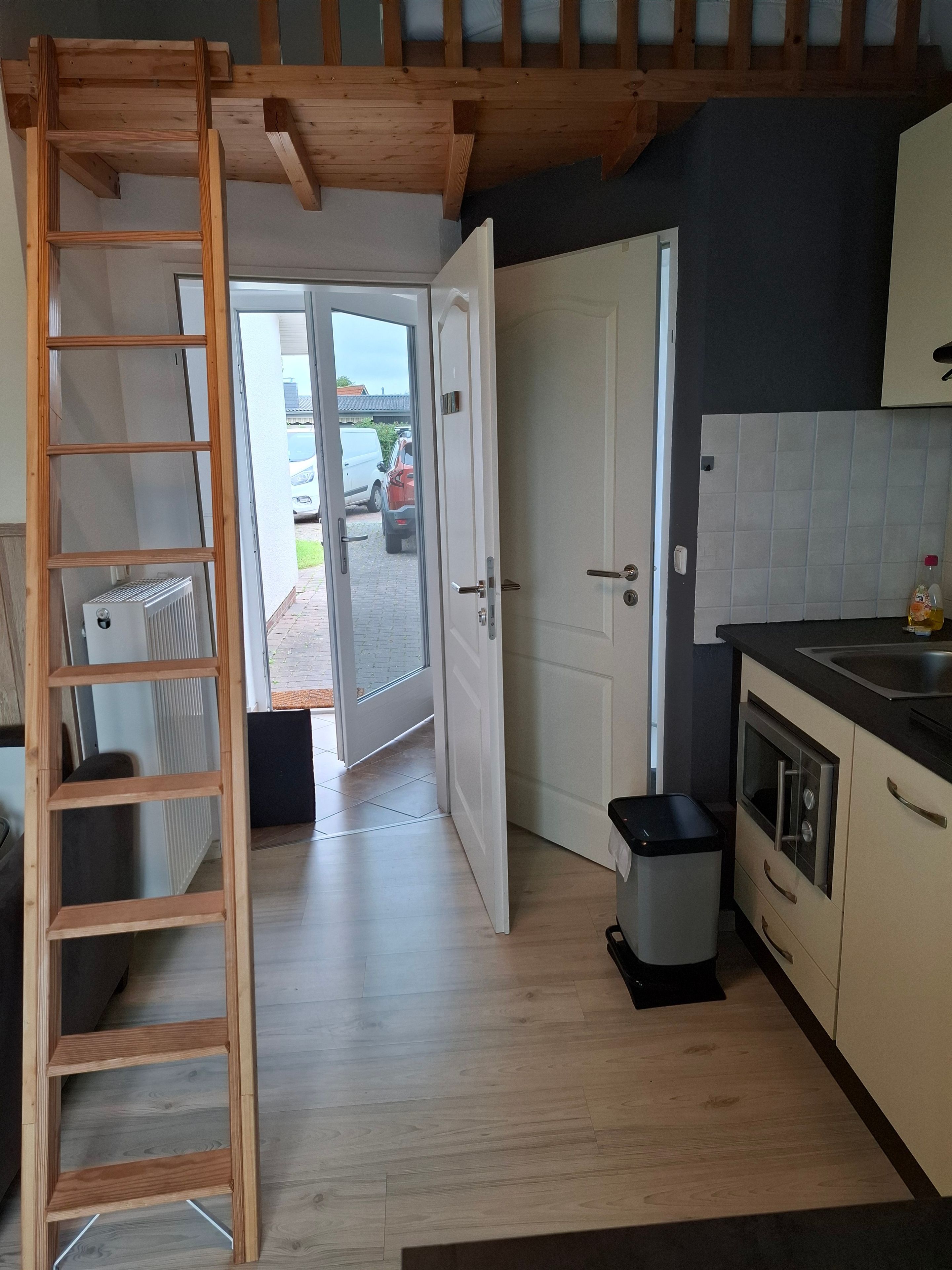 Eine Küche mit einer Holzleiter, einer offenen Tür, die nach draußen führt, einer Mülltonne und einem eingebauten Backofen.
