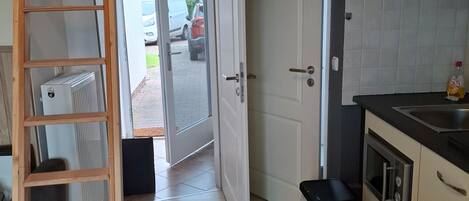 A kitchen with a wooden ladder, an open door leading outside, a trash bin, and a built-in oven.