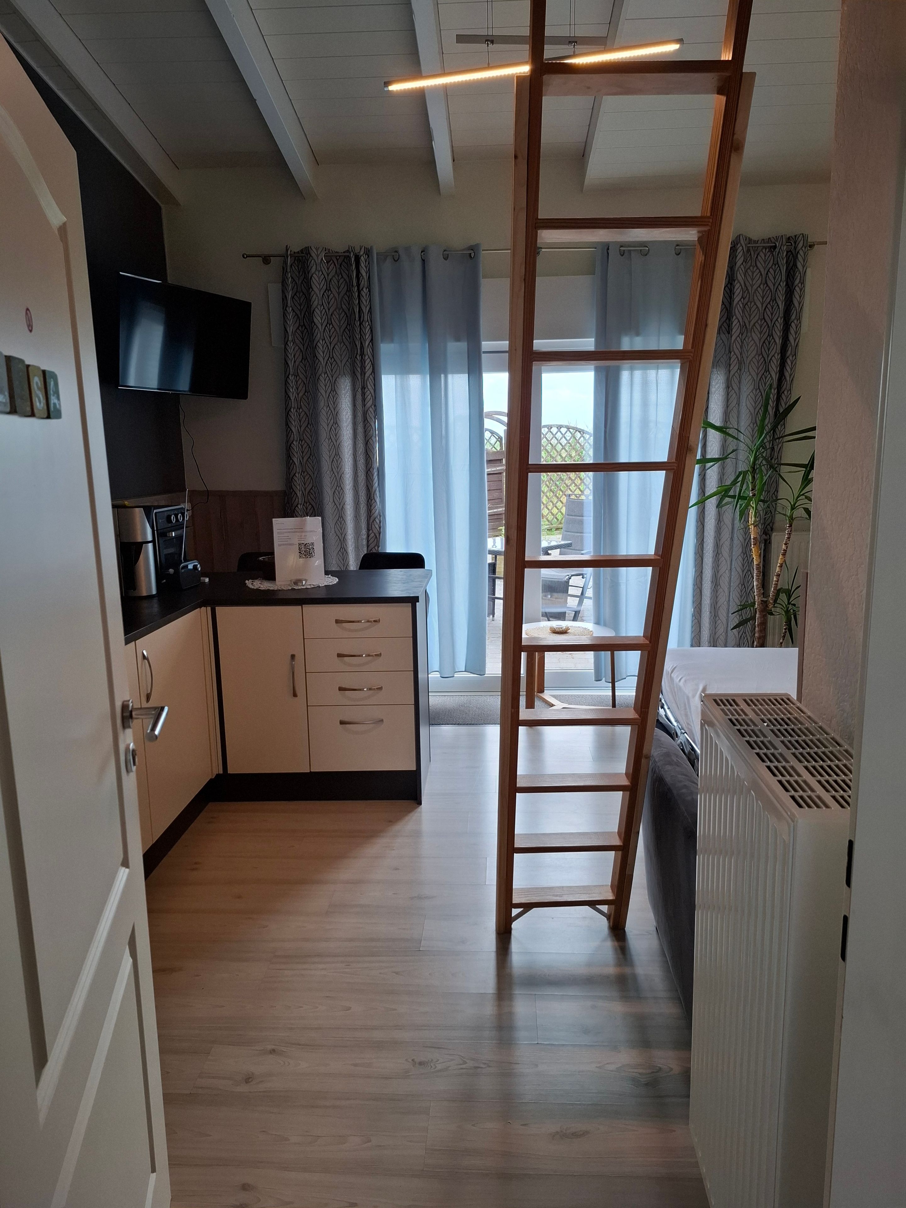 A modern kitchen with wooden cabinets, a built-in oven, and a flat-screen TV.