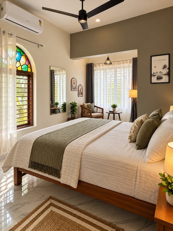 A bedroom with a bed, a ceiling fan, a window with curtains, a bedside table with a lamp, and a framed picture on the wall. - The Village House (Varkala)
