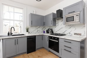 A modern kitchen with grey cabinets, a black dishwasher, a built-in oven, and a microwave. - Stylish West London Home,Superking Bed, Workspace, Garden & Great Travel Connect (London)