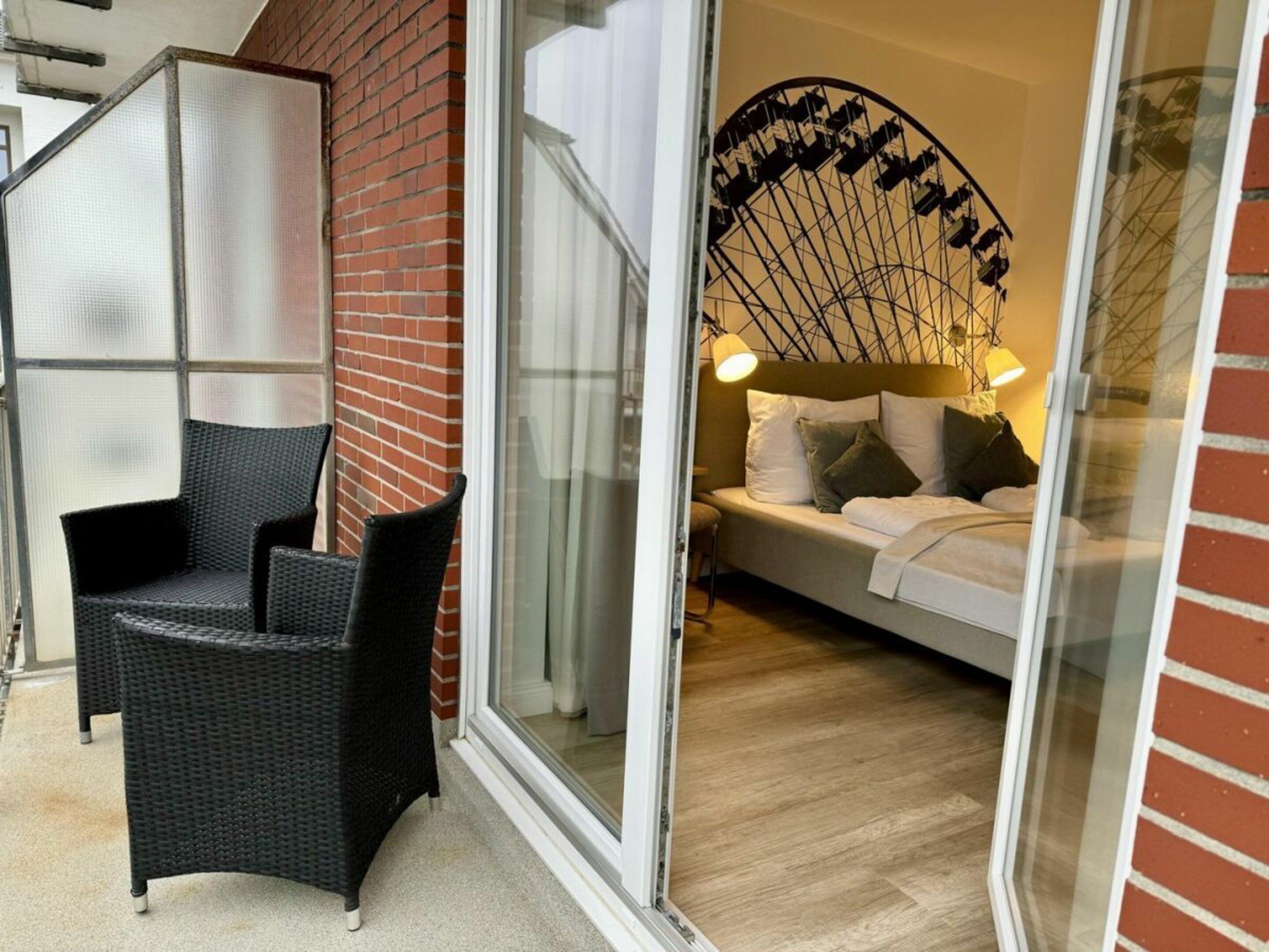 Una habitación con cama, una silla y un ventanal que da a un balcón.