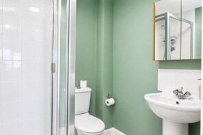 A bathroom with a glass shower enclosure, a white toilet, and a white sink with a chrome faucet. - Stylish 2-Bed, 2-Bath Flat with Balcony & Parking (Warrington)
