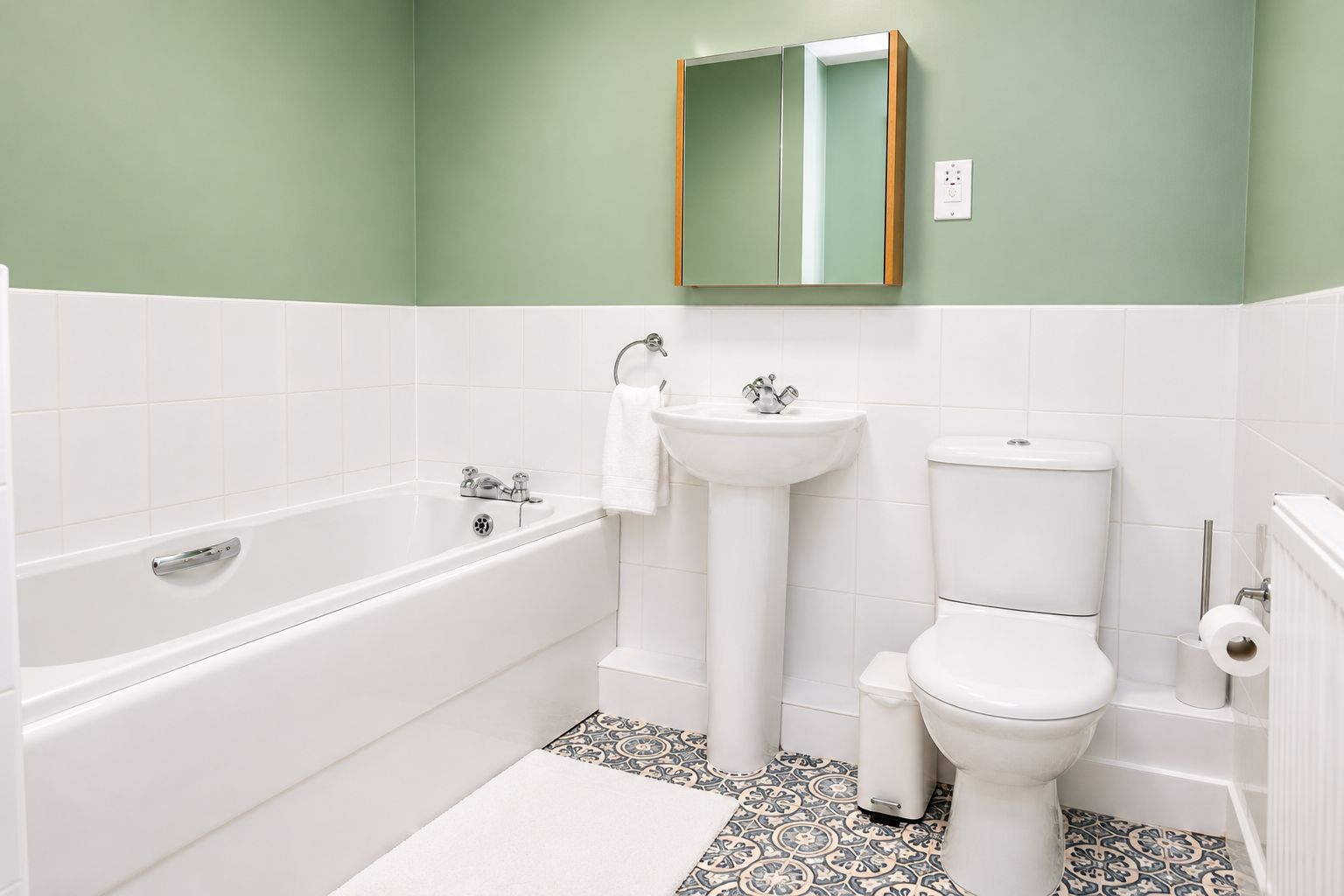 A bathroom with a bathtub, sink, and toilet, featuring white fixtures and patterned floor tiles.