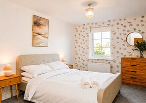 Un dormitorio con cama, mesitas de noche, cómoda, ventana y candelabro.