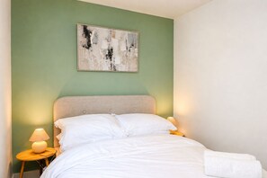 A neatly made bed with white linens, a headboard, and a bedside lamp on a wooden nightstand. - Stylish 2-Bed, 2-Bath Flat with Balcony & Parking (Warrington)