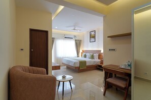 A hotel room with a bed, a desk, a chair, a round table, and a door. - The Royal Suites (Bengaluru)