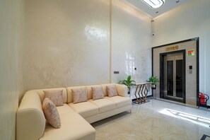 A modern lobby with a beige sofa, a reception desk, and an elevator. - The Royal Suites (Bengaluru)