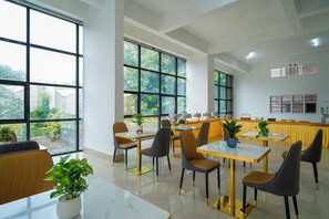 A modern dining area with large windows, multiple tables, and chairs. - The Royal Suites (Bengaluru)