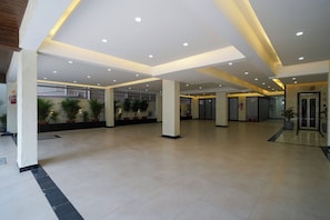 A spacious lobby with a high ceiling, recessed lighting, and potted plants. - The Royal Suites (Bengaluru)