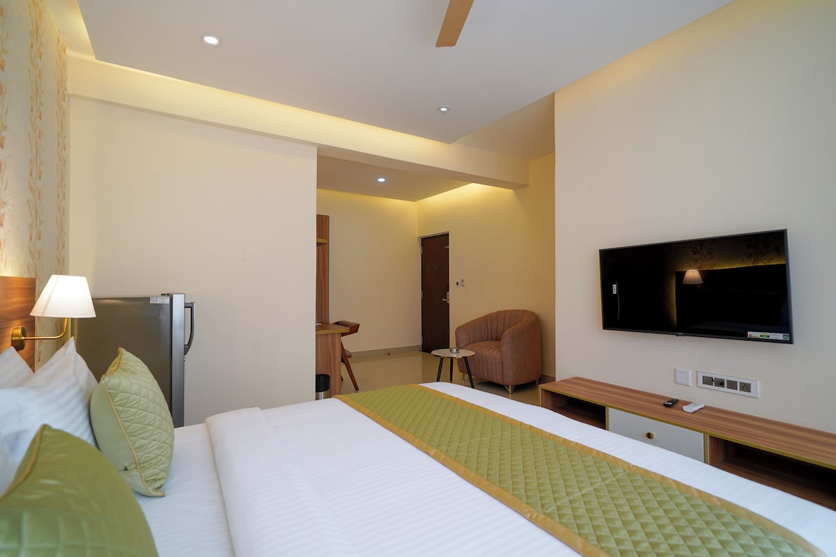 A hotel room with a bed, a desk, a chair, a television, and a refrigerator.