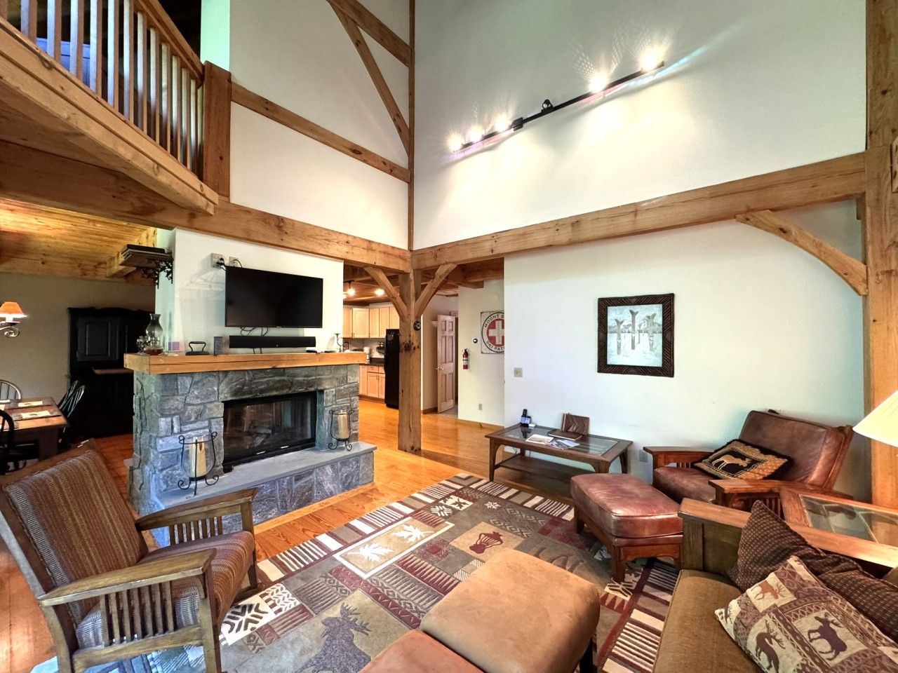 A spacious living room with a stone fireplace, wooden beams, and a television mounted above it.
