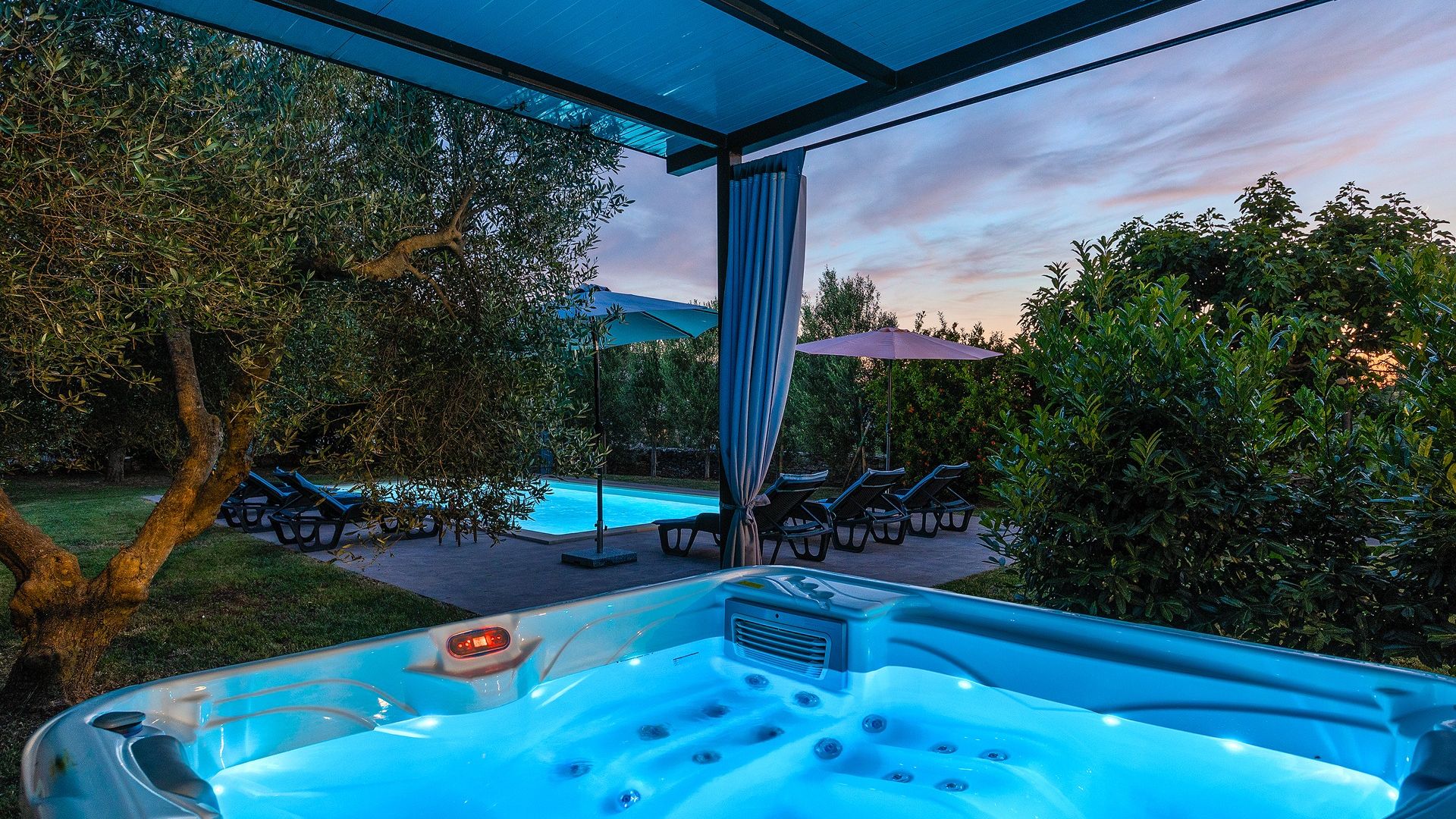 Un bain à remous avec vue sur une piscine et des chaises longues, le tout entouré de verdure.