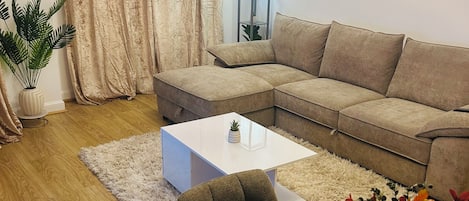A modern living room with a sectional sofa, a dining table set for two, and a large window with curtains.