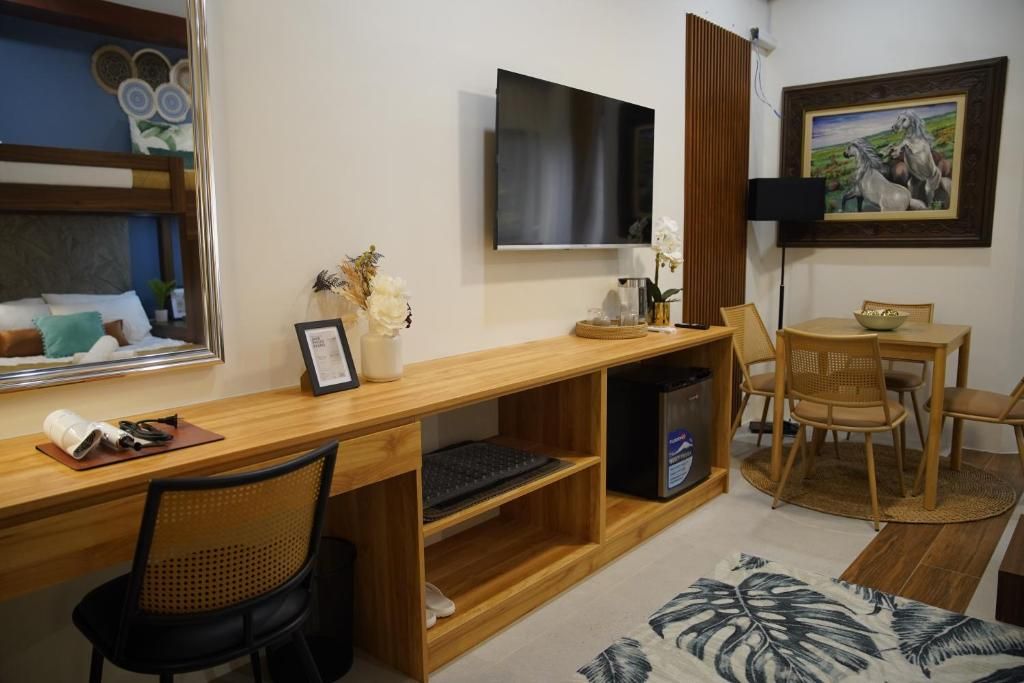 Una habitación con un escritorio de madera, una silla, un televisor, un cuadro enmarcado y un comedor con sillas y una mesa.