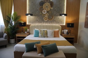 A hotel room with a large bed, two bedside tables, a potted plant, and a decorative wall piece. - Isla Mystica Beach Resort (San Juan)