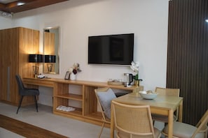 Una sala moderna con un escritorio de madera, un televisor montado en la pared y un comedor con sillas de mimbre.