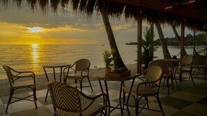A beachside cafe with wicker chairs and tables, overlooking the ocean at sunset. - Isla Mystica Beach Resort (San Juan)