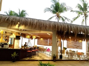 An outdoor seating area with a thatched roof, checkered floor, and palm trees in the background. - Isla Mystica Beach Resort (San Juan)