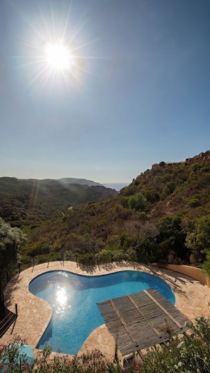 A swimming pool with a stone deck, surrounded by lush greenery and hills. - Kind & Secret:  villa with pool and panoramic rooftop terrace (Costa Paradiso)