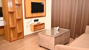 Una sala de estar con un televisor de pantalla plana montado en la pared, una mesa de centro de vidrio, un sofá y una estantería de madera.