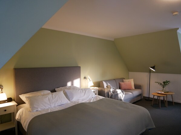 A hotel room with a bed, bedside table, lamp, and a small table with a plant. - Ferienhof Hage (Hüde)